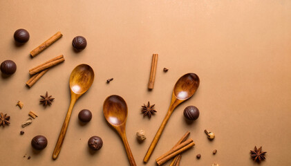 Wooden spoons with chocolate truffles, cinnamon sticks, and spices on brown background