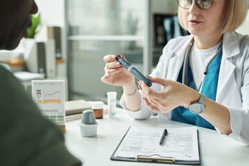 Middle aged Caucasian female doctor demonstrating blood glucose meter to middle aged Black man...