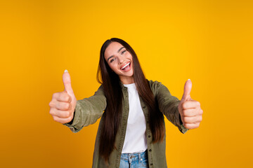 Young woman smiling on yellow background with thumbs up sign, expressing positivity with casual...