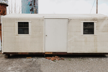 Corrugated metal portable building with central door and flanking windows on gravel base with...