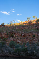 Side of Chamberlain Gorge red rock wall with trees on top Chamberlain Gorge in postcard perfect scene.