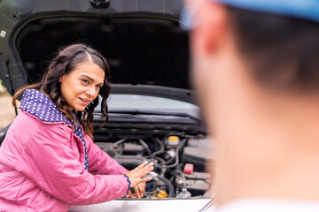Woman checking car engine with mechanic assisting