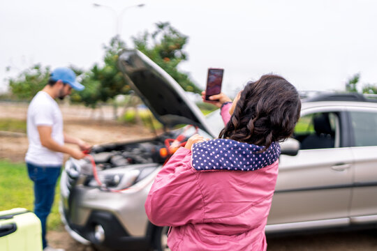 Woman taking photo of mechanic fixing her car on roadside