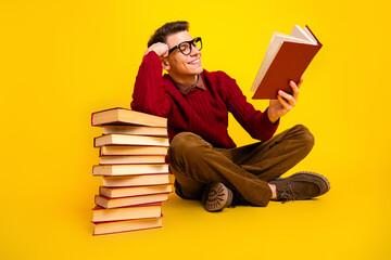 Young Male Reading Book While Sitting with Stack of book on Yellow Background