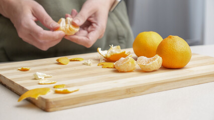 Hands peeling of orange tangerines on the cutting board on table, lots of juicy fresh fruits for...