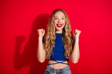 Joyful young woman with long blonde hair, wearing a blue top, enthusiastically expresses happiness...
