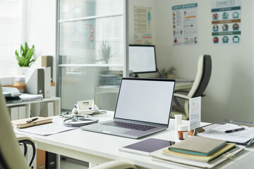 Medical office desk displaying laptop, digital blood glucose meter, stethoscope, prescription bottles, diabetes educational materials, posters about diabetes care on wall
