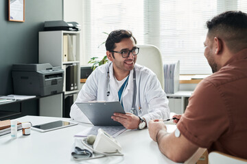 Middle aged Caucasian male doctor smiling while consulting middle aged Hispanic man with diabetes...