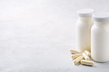 Bottles of white milk yogurt (kefir) and capsules with probiotic on a light background. The concept of an alternative to pills and a healthy diet