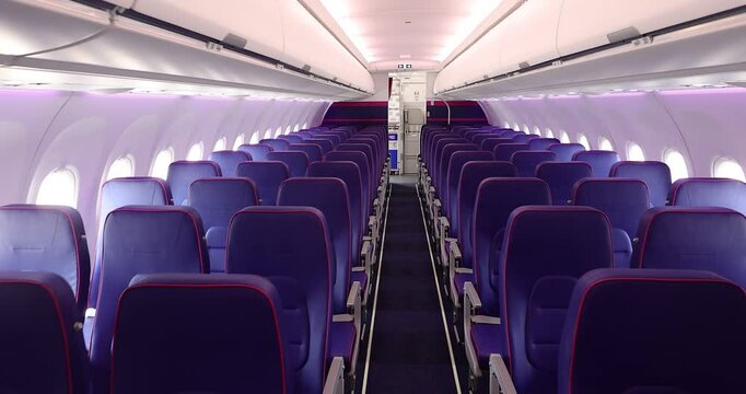4K video of empty interior of new modern airplane Airbus A321 XLR with blue seats and no passangers. Photographed in ambiental light. Selective focus.