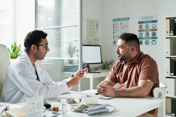 Middle aged Caucasian man sitting across from male doctor in medical office discussing diabetes...