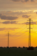 Two tall, elegant power lines are beautifully silhouetted against the stunning hues of a sunset sky...
