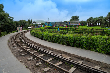 Fototapeta premium Darjeeling,West Bengal,India - 20.08.2023 : Diesel Toy train passing through curvy Himalayan road. Darjeeling Himalayan Railway, narrow gauge railway. Unesco world heritage site, Himalayan monsoon.