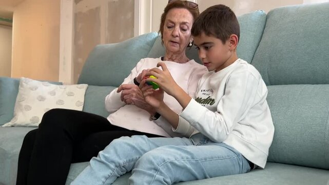 Boy playing with colorful puzzle cube next to elderly woman on living room couch in a peaceful intergenerational bonding moment