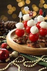 Tasty canapes and Christmas decor on wooden table against background with blurred lights, closeup. Bokeh effect