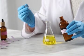 Professional perfumer developing luxury perfume at white wooden table in laboratory, closeup