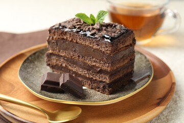 Piece of delicious chocolate cake with mint and tea on table, closeup
