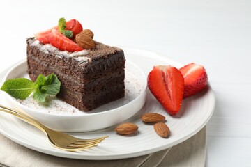 Piece of delicious chocolate cake with strawberries, almonds and mint on white table, closeup