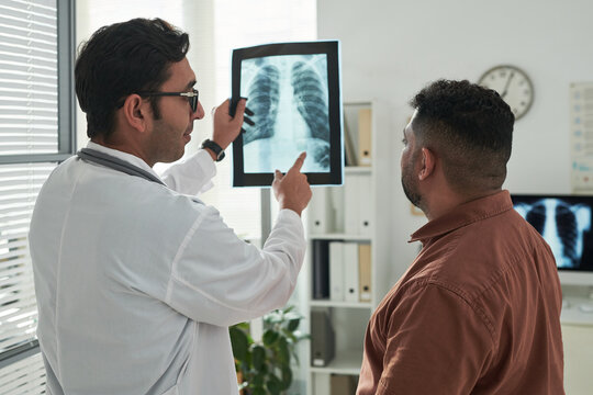 Middle aged Caucasian male doctor showing chest X ray to middle aged Hispanic man during diabetes consultation in medical office, both standing and discussing diagnostic results
