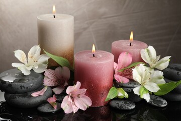 Burning candles, spa stones and beautiful flowers on wet black table, closeup