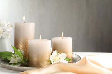 Burning candles and beautiful flowers on white table. Space for text