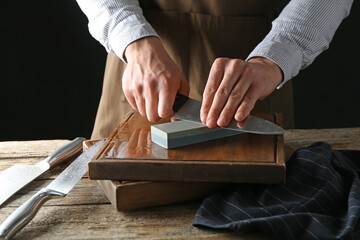 Man sharpening knife with sharpener on wooden table, closeup