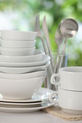 Different clean dishes on white table against blurred green background, closeup