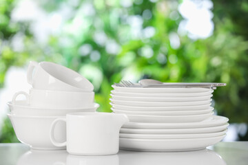 Different clean dishes on white table against blurred green background
