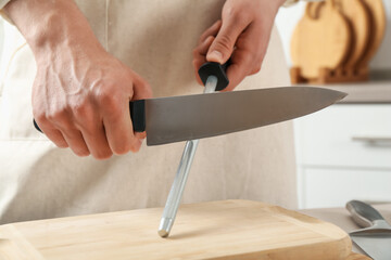 Man sharpening knife with sharpener at table indoors, closeup