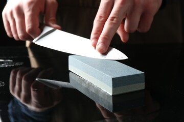 Man sharpening knife with sharpener at mirror table, closeup