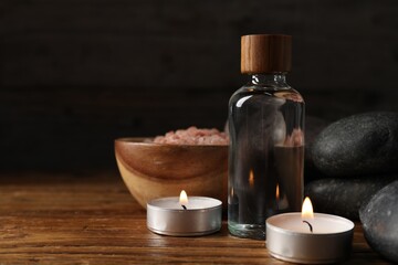 Spa composition with cosmetic products and burning candles on wooden table against black background, closeup