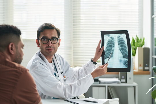 Middle aged Caucasian male doctor explaining chest X-ray results to middle aged man during diabetes consultation in medical office, doctor holding X-ray and pointing at image