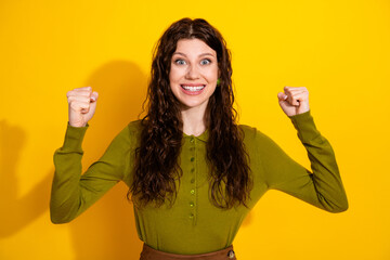 Young woman in a green shirt expressing excitement with raised fists over a yellow background