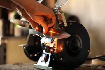 Man sharpening knife with bench grinder indoors, closeup