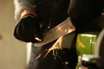 Man sharpening knife with bench grinder indoors, closeup