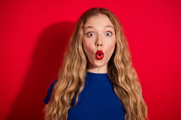 Surprised young woman expressing astonishment against vibrant red background wearing a blue top...