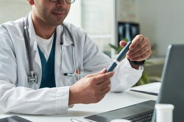 Middle aged Caucasian male doctor holding insulin pen while consulting patient with diabetes in...
