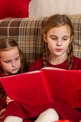 Two little sisters snuggling up on the sofa in a cozy living room at Christmas at home during...