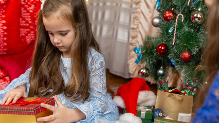 A beautiful little girls in a fluffy festive dress gets surprised with a gift in a Christmas...