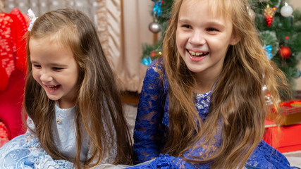 A happy little girls in a beautiful blue dress sitting in festive Christmas interior with a gifts...