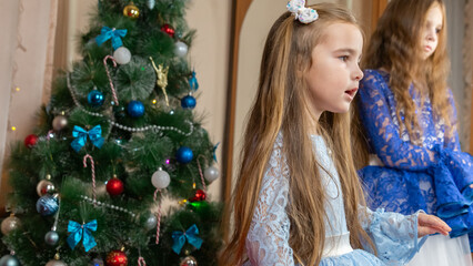 Little girls in festive dress dancing near christmas tree at home