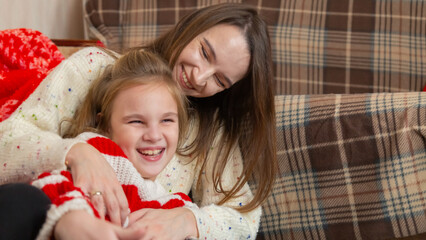 Happy family having fun at home for Christmas. Mother tickles her daughter sitting on the floor....