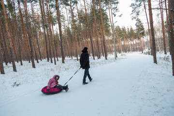 Dad with his daughter walking with snow tubing in the winter forest
