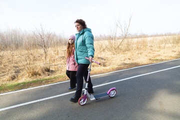 Little girl riding scooter while walking with her grandmother in the forest on a sunny day