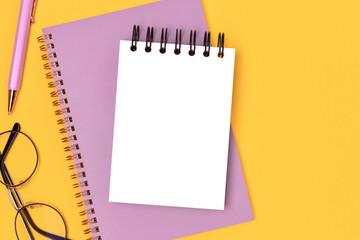 Workspace with clean notepad mockup and purple colored stationery on a yellow background. Notebook template.