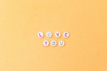 Love you. Quote made of white round beads with multicolored letters on a golden background.