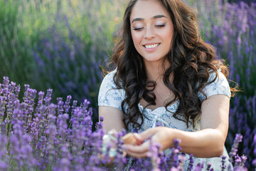 Young beautiful woman picking lavender flowers in the field. Holding a jar of essential oil in her...