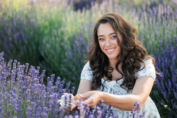 Young beautiful woman picking lavender flowers in the field. Holding a jar of essential oil in her...