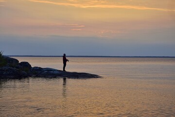 Fisherman with a fishing rod on the lake shore in the evening. Hobbies and recreation.