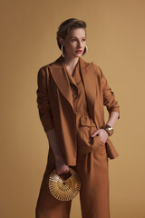 Elegant woman in rust-colored suit posing confidently with wooden clutch against warm-toned background.